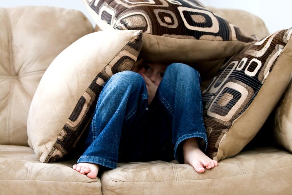 Boy hiding under pillows on couch, perhaps sad or suffering from anxiety