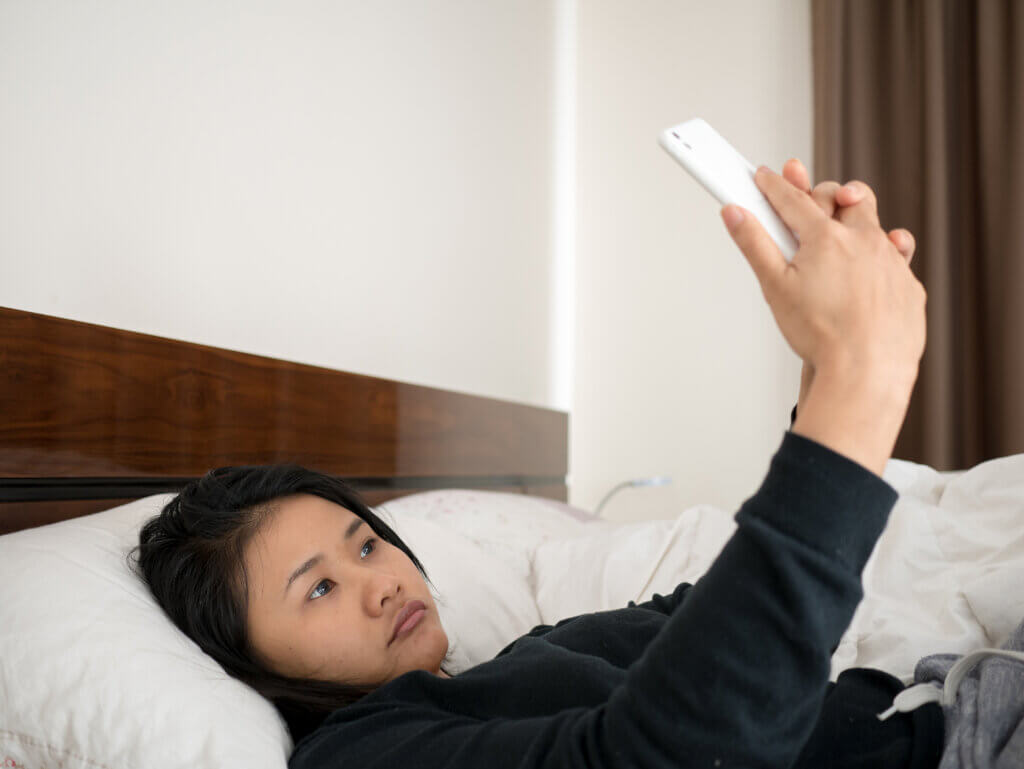 Sad woman lying in bed taking selfie with smartphone