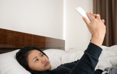 Sad woman lying in bed taking selfie with smartphone
